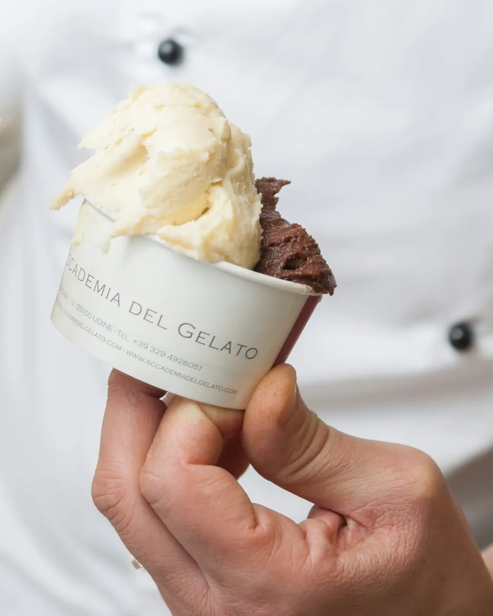 Una coppetta di gelato con il logo dell'Accademia del Gelato, in mano al gelatiere